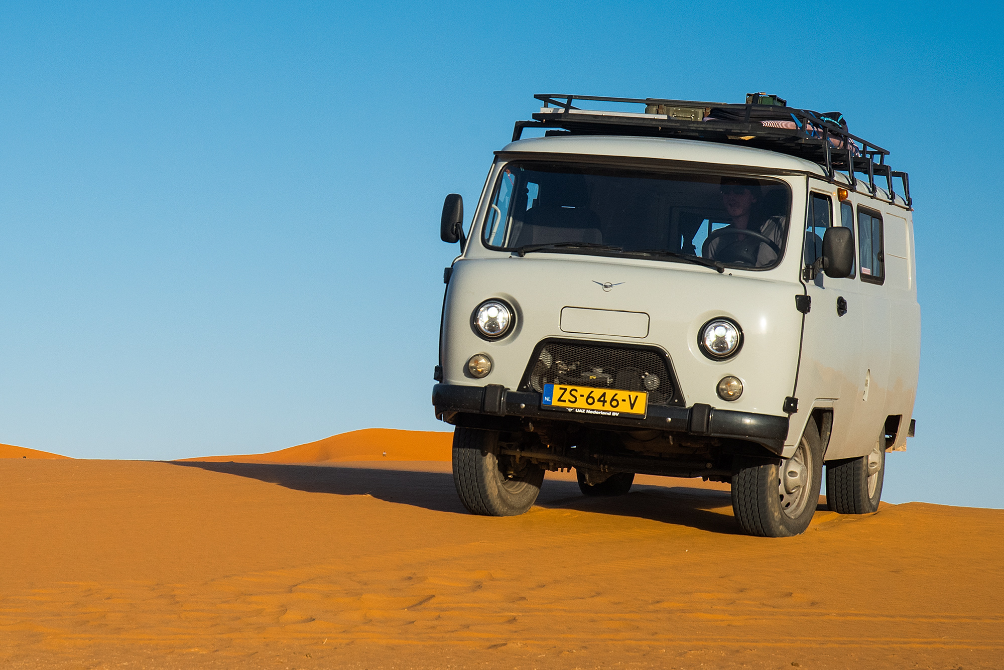 Een UAZ Bukhanka rijdt offroad door de woestijn in de Marokkaanse Sahara